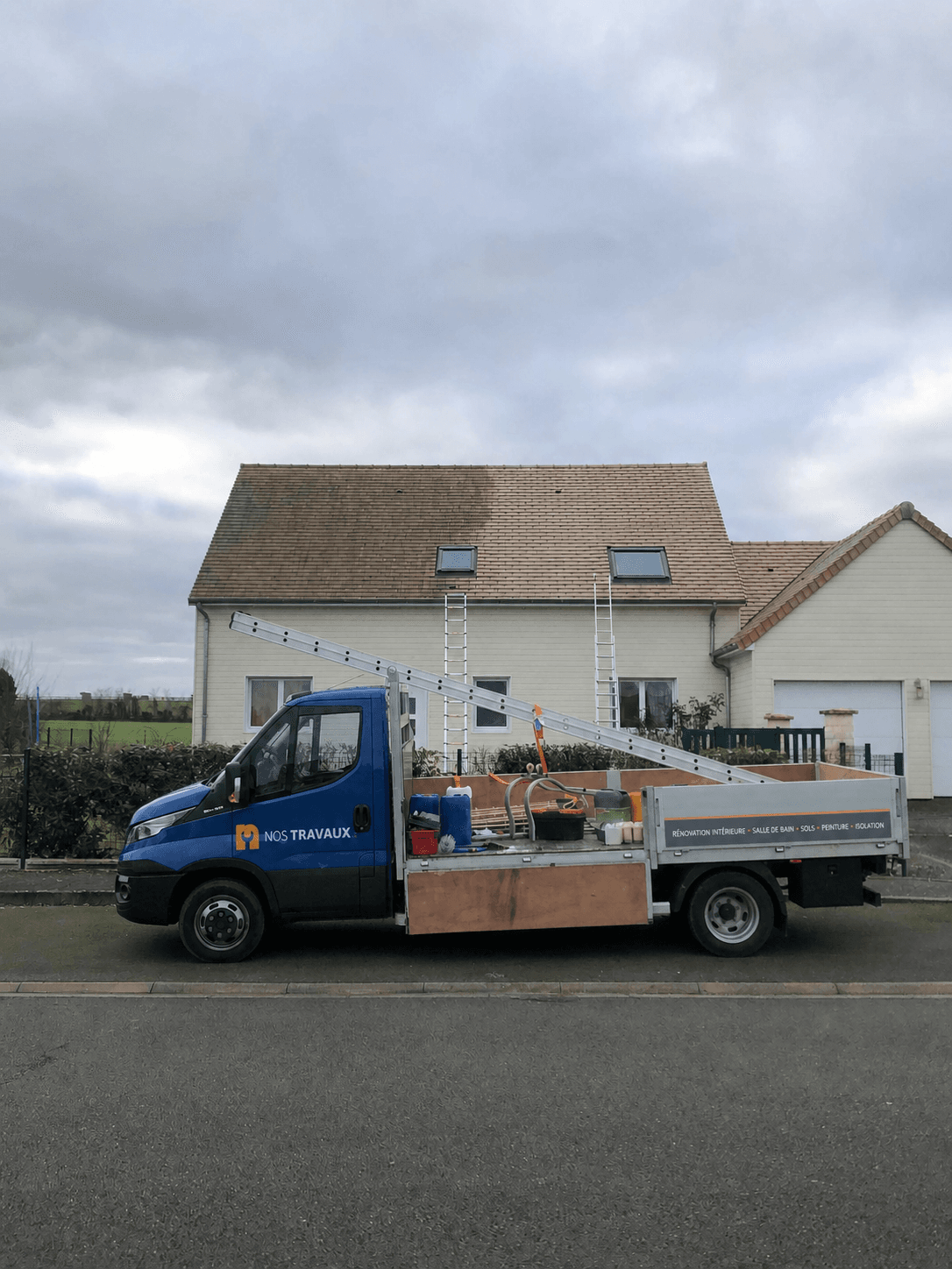 Camion plateau Nos Travaux devant une maison en travaux
